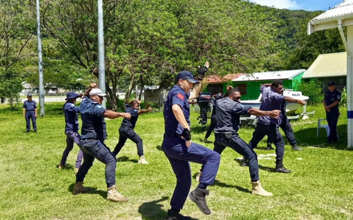 7 men in navy police uniform adopt wide stances with one raised knee and arms while training outdoors on grass