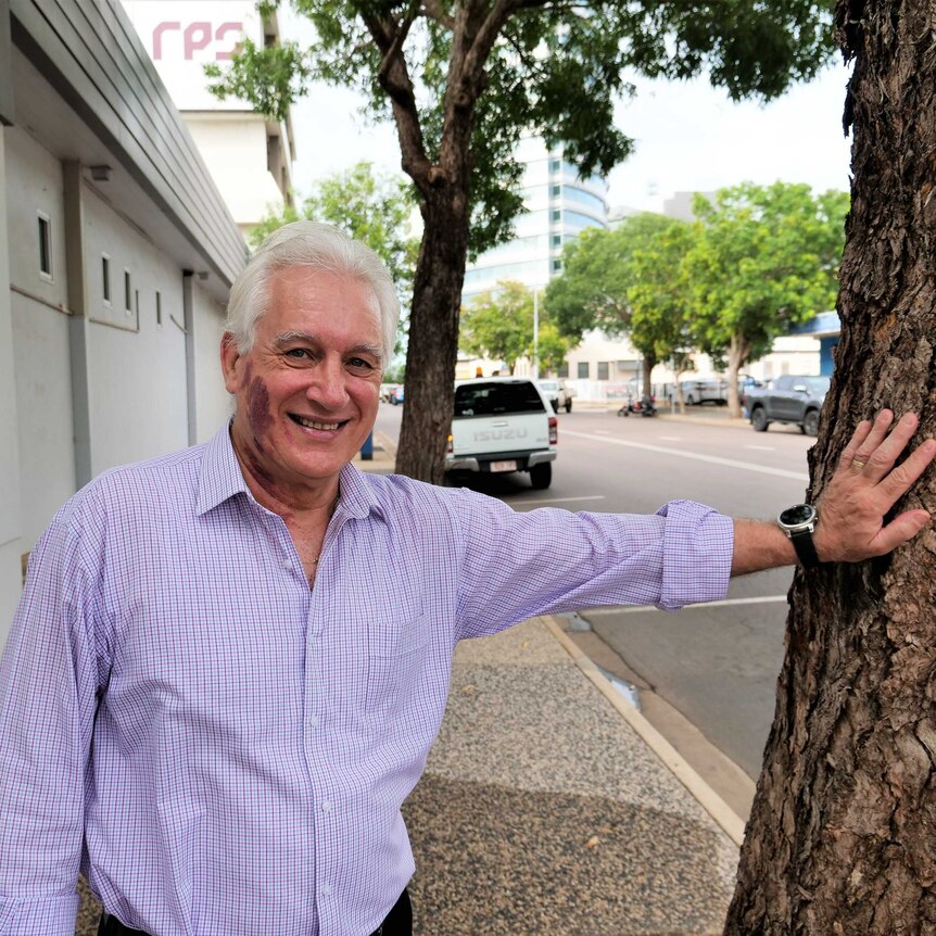 Darwin Lord Mayor Kon Vatskalis fresh from coronavirus self-isolation leaning against a tree