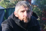 A homeless man sits at a makeshift campsite in the bush