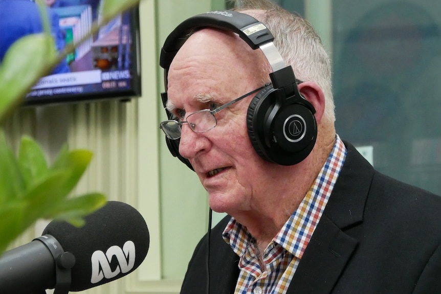 Tom Wyatt, with headphones half on, talks into a microphone in a radio studio