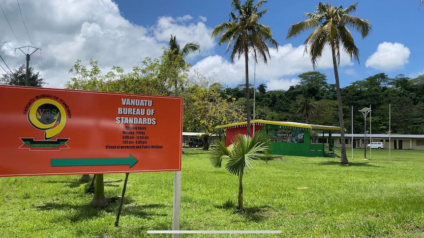 Two signs on a lush green lawn with palm trees in the background