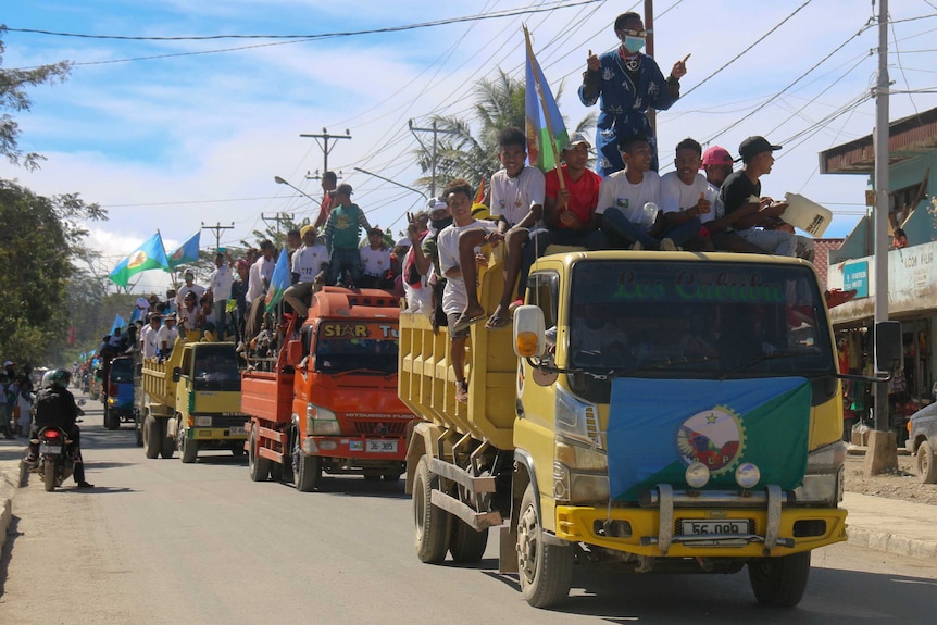 Young supporters piled on top of colourful orange and yellow trucks, waving flags, head to an election rally in Aileu district.