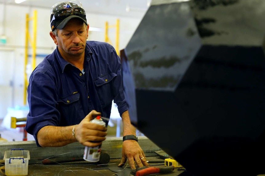 A man uses a spray can on a piece of art made of metal