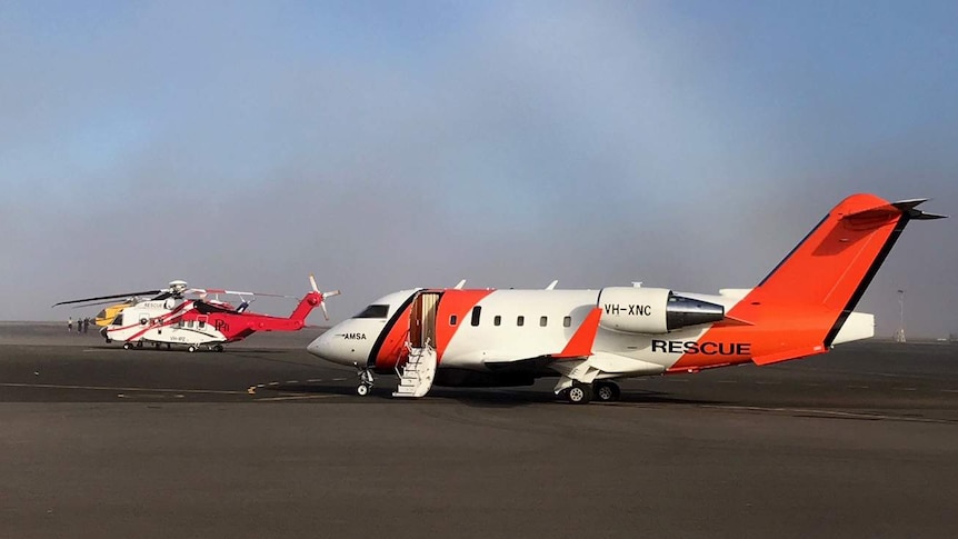 An AMSA jet and a rescue helicopter sit on the tarmac under grey skies.