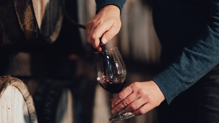 hands pouring port into a glass from the hose of a barrel 