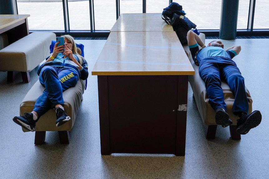 Гравці збірної України лежать на стільцях на парті, один читає свій iPhone, а інший дивиться ліворуч