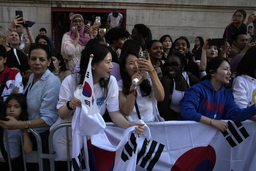 A crowd of fans behind a barricade holding signs and phones