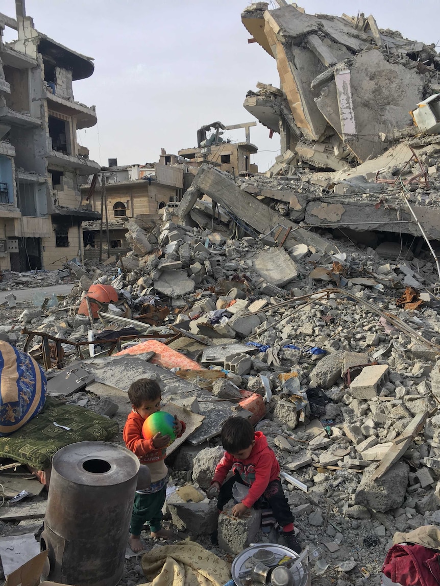 Children including one holding a ball searching in rubble in Raqqa.