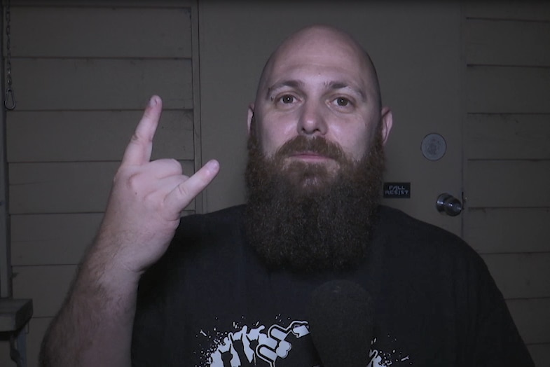 Bald man with big beard makes devil horns sign.