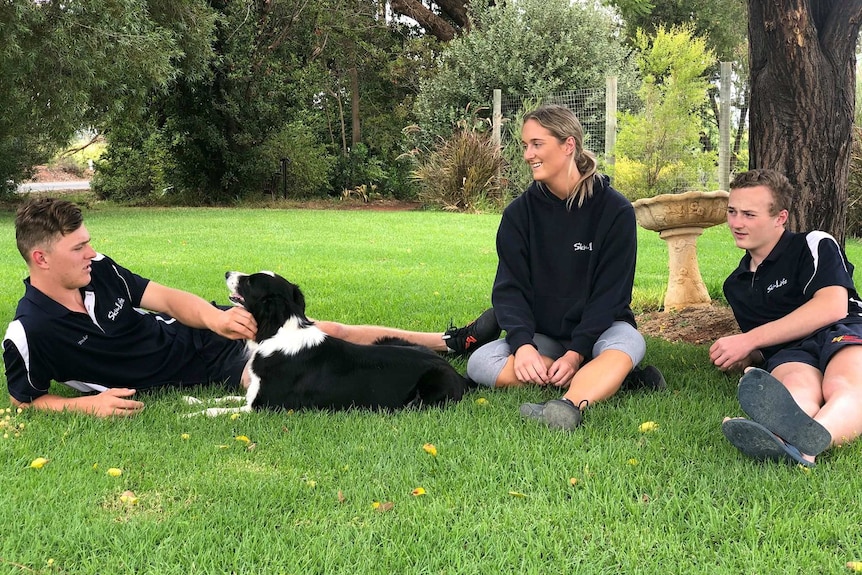 Three people sitting on the ground with a dog