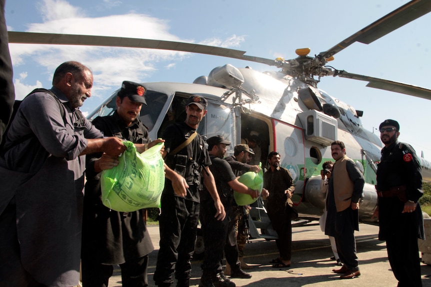 Officials pass plastic bags full of goods to a crew that is loading them into a helicopter for delivery to flooded areas.