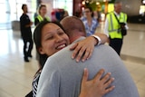 Catherine smiles widely as she hugs her husband, airport staff are visible in the background.