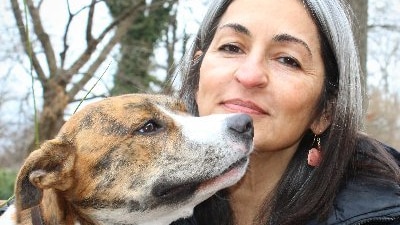 woman with grey and black hair with a brown and white dog's head near her face