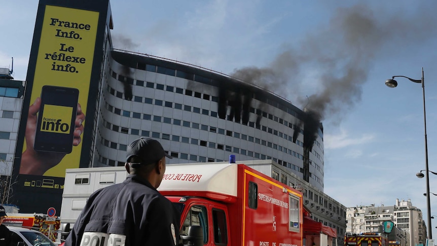 A policeman stands near fire trucks as smoke rises from windows at the Maison de la Radio station on October 31, 2014.