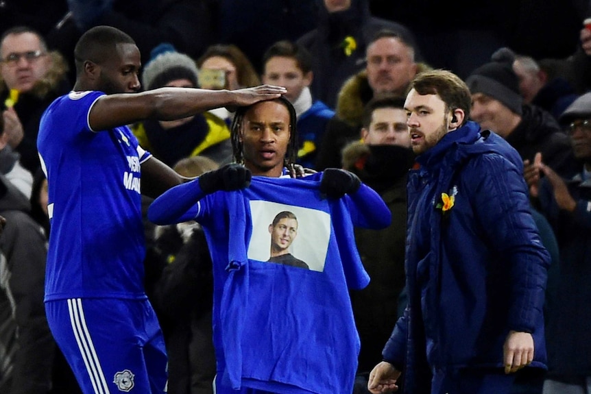 Football players in blue jerseys holding a t-shirt with a picture of the missing footballer