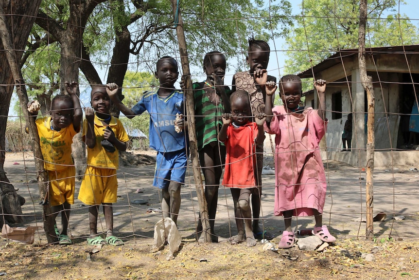 Displaced South Sudanese children peer through a wire fence