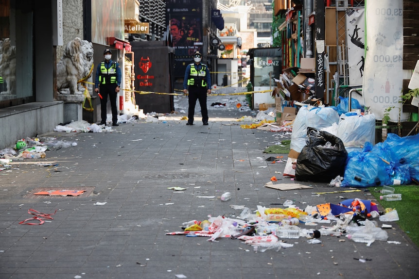 An alley filled with rubbish, guarded by two police officers
