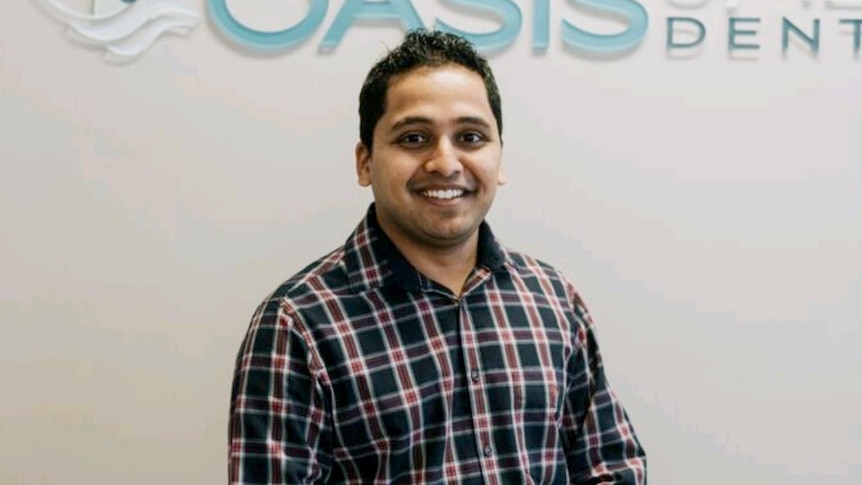 man smiling at camera in front of oasis dental clinic sign