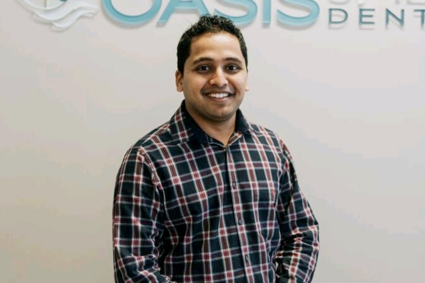 man smiling at camera in front of oasis dental clinic sign