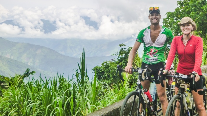 Donna and her husband Nick with their bicycles, in front of the lush green mountains of Ecuador.