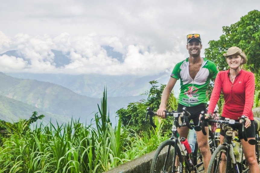 Donna and her husband Nick with their bicycles, in front of the lush green mountains of Ecuador.