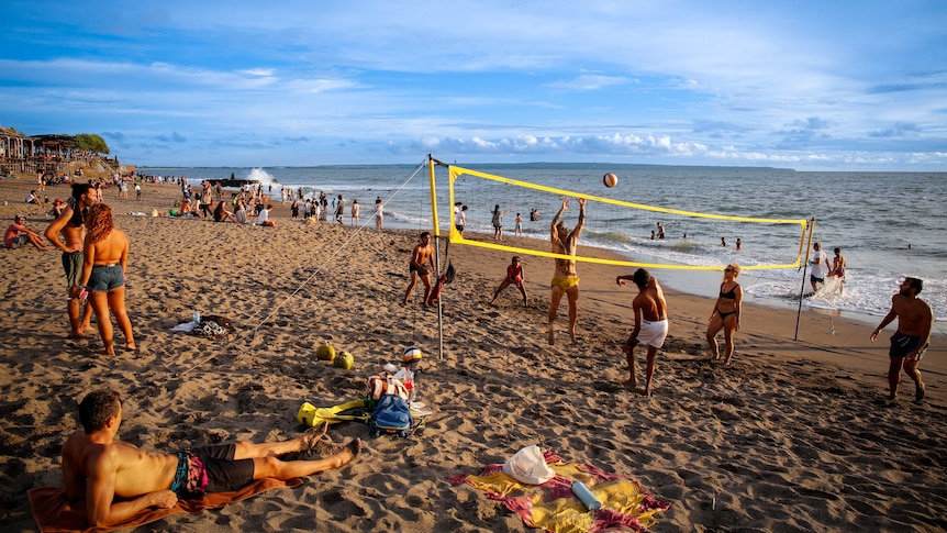 People laying around and playing volleyball on a tropical beach