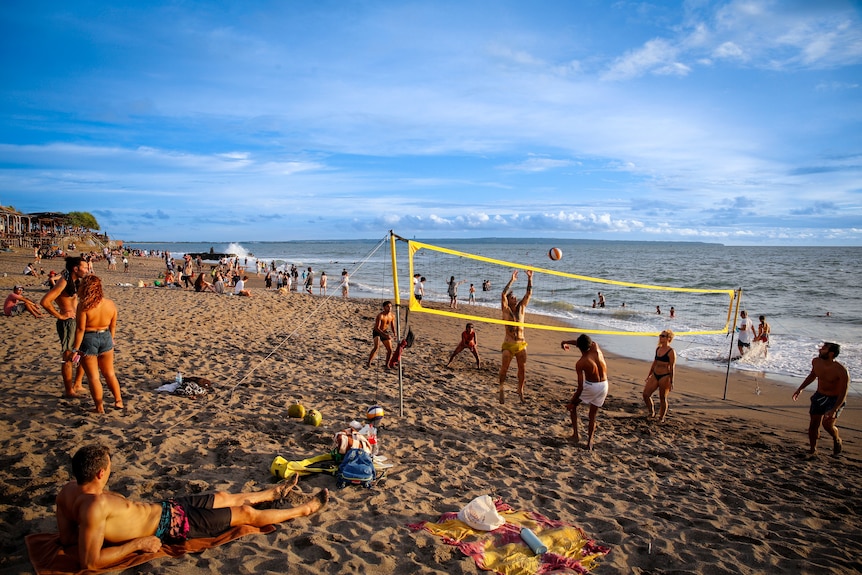 People laying around and playing volleyball on a tropical beach