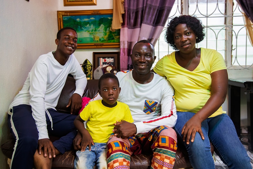 Victor Erebifa Phullu (center) with wife Maria, daughter Emmanuella, and his nephew Emmanuel sit on the couch together