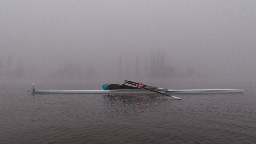 A rower succumbs to the fog and exhaustion by lying down.