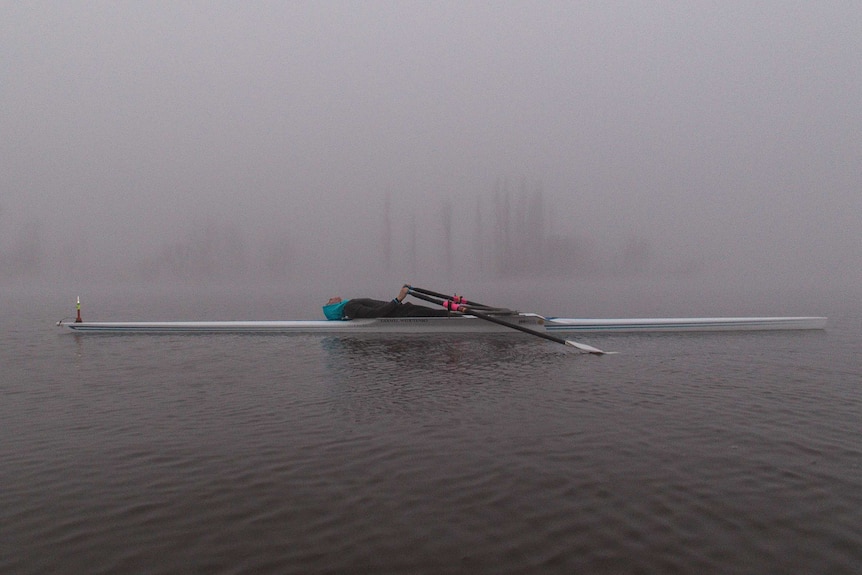 A rower succumbs to the fog and exhaustion by lying down.