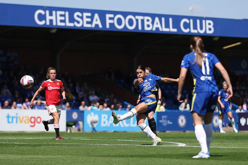 A female soccer player in blue takes a powerful shot with the words 'Chelsea Football Club' behind her