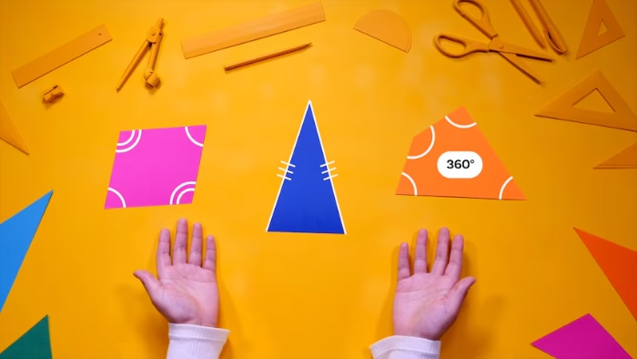 Two hands gesture towards graphics of triangles and quadrilaterals on a yellow desk.