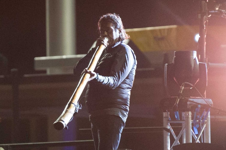 A man on stage plays the didgeridoo.