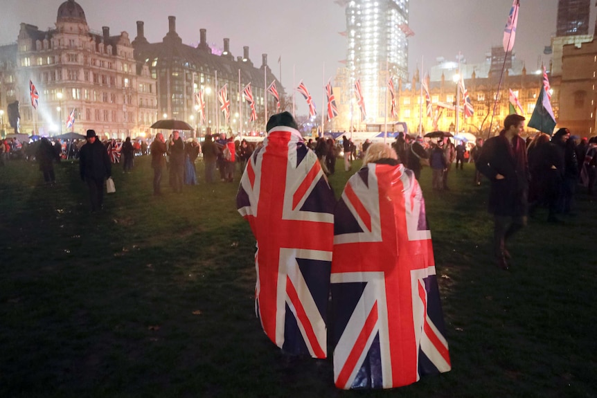 People draped in UK flags walks across Parliament Square during a rainfall in London.