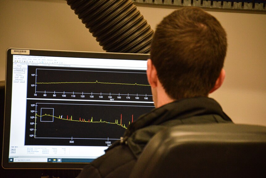A man sits with his back to the camera as red and yellow graphs appear on the computer screen