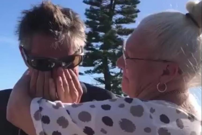 Upset man with hands over eyes is consoled by woman with grey hair.