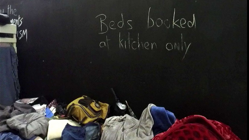 Sign on hoarding at makeshift camp for homeless: "Beds booked at kitchen only"