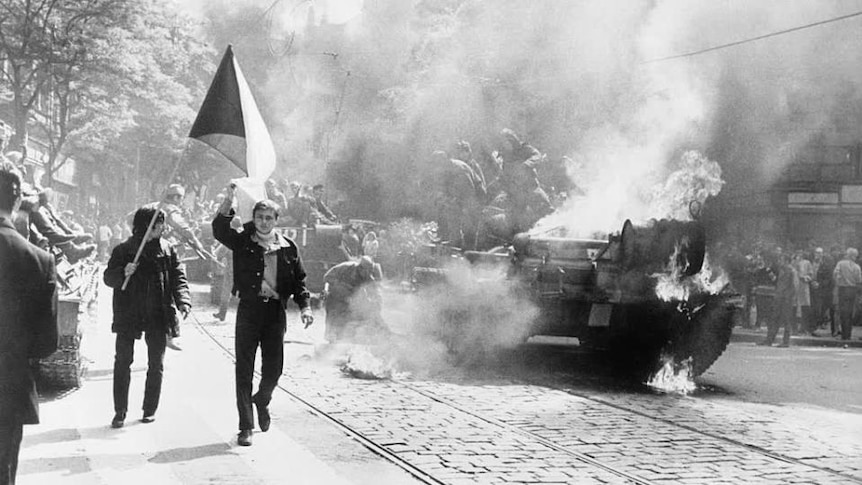 Photo of protestors standing beside a burning tank