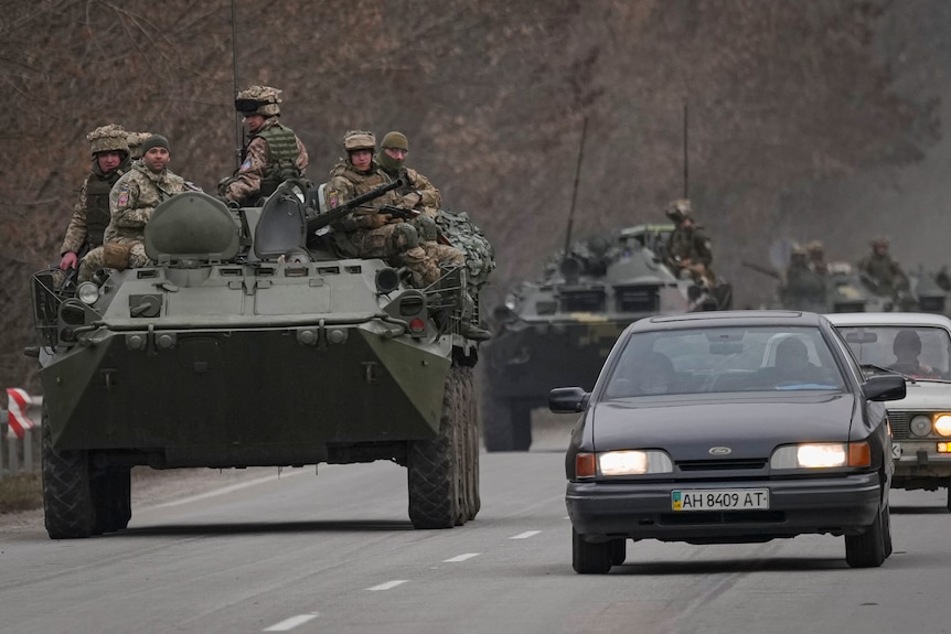 A road has one lane filled with regular traffic and one lane filled with tanks covered with soldiers