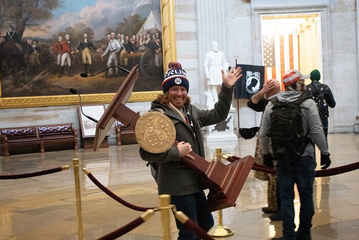 A rioter smiling as he carries off a lectern from the House of Representatives.