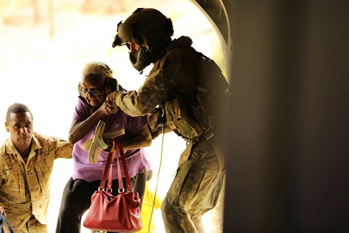 A soldier helps a lady onto the aircraft