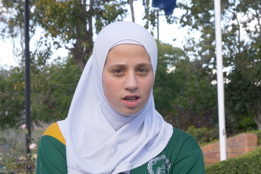 A schoolgirl wearing a head covering poses for a photograph with a serious expression.