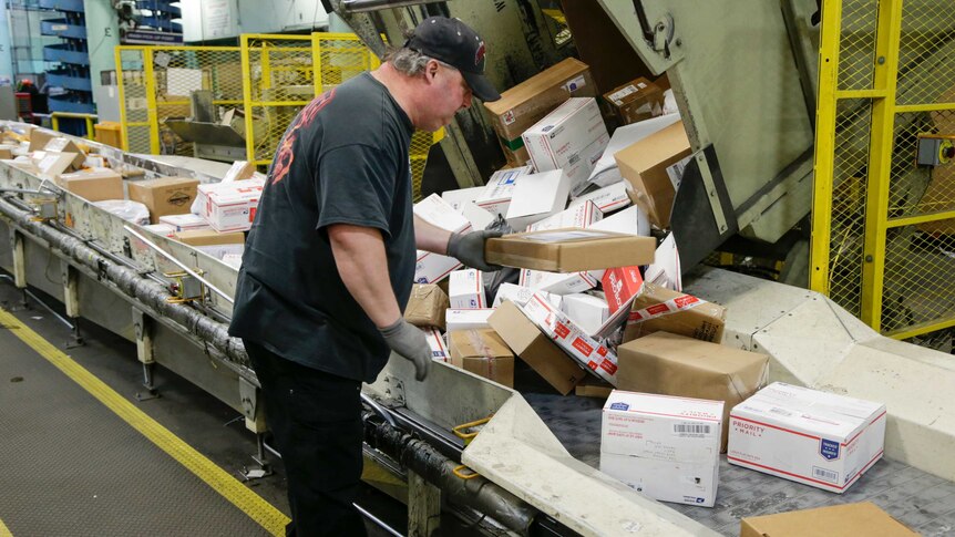 A man sorts parcels on a conveyer belt.