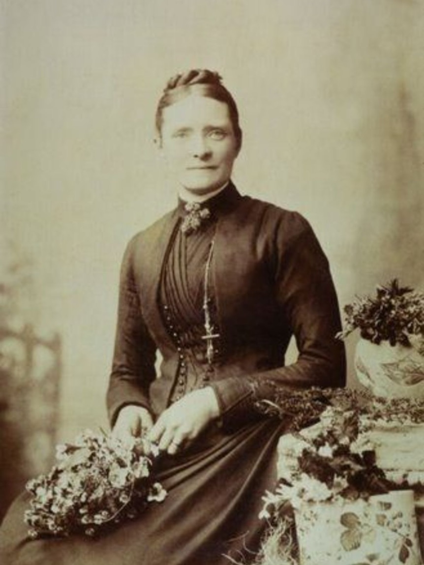 A black and white photo of a woman in period dress holding flowers.