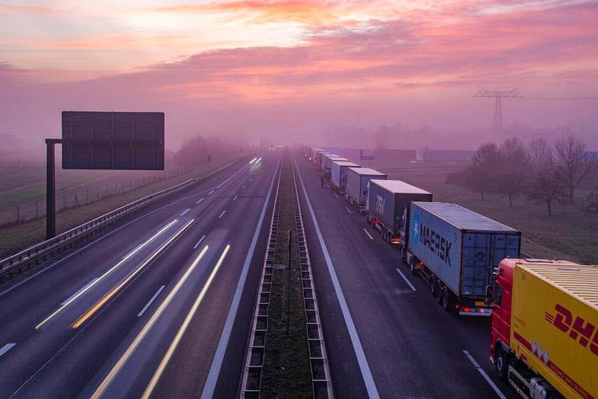On a bright pink morning, you see a line of trucks on an otherwise empty Autobahn.