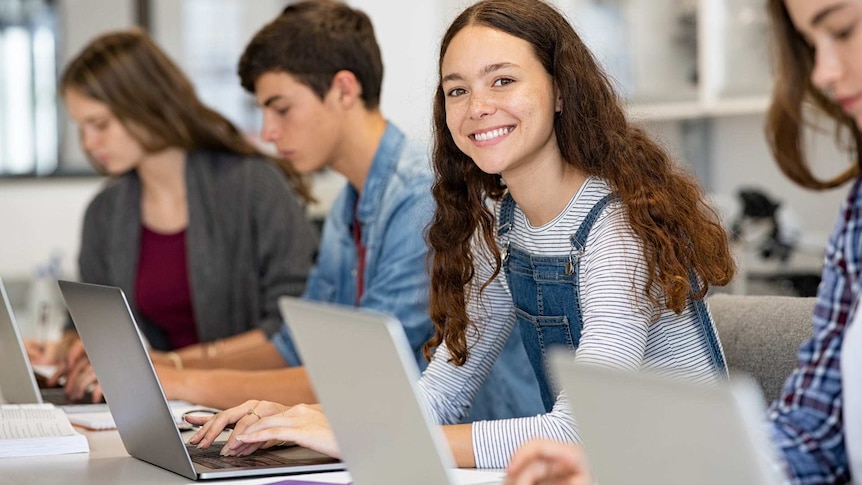 A happy high school girl using a laptop in a classroom.