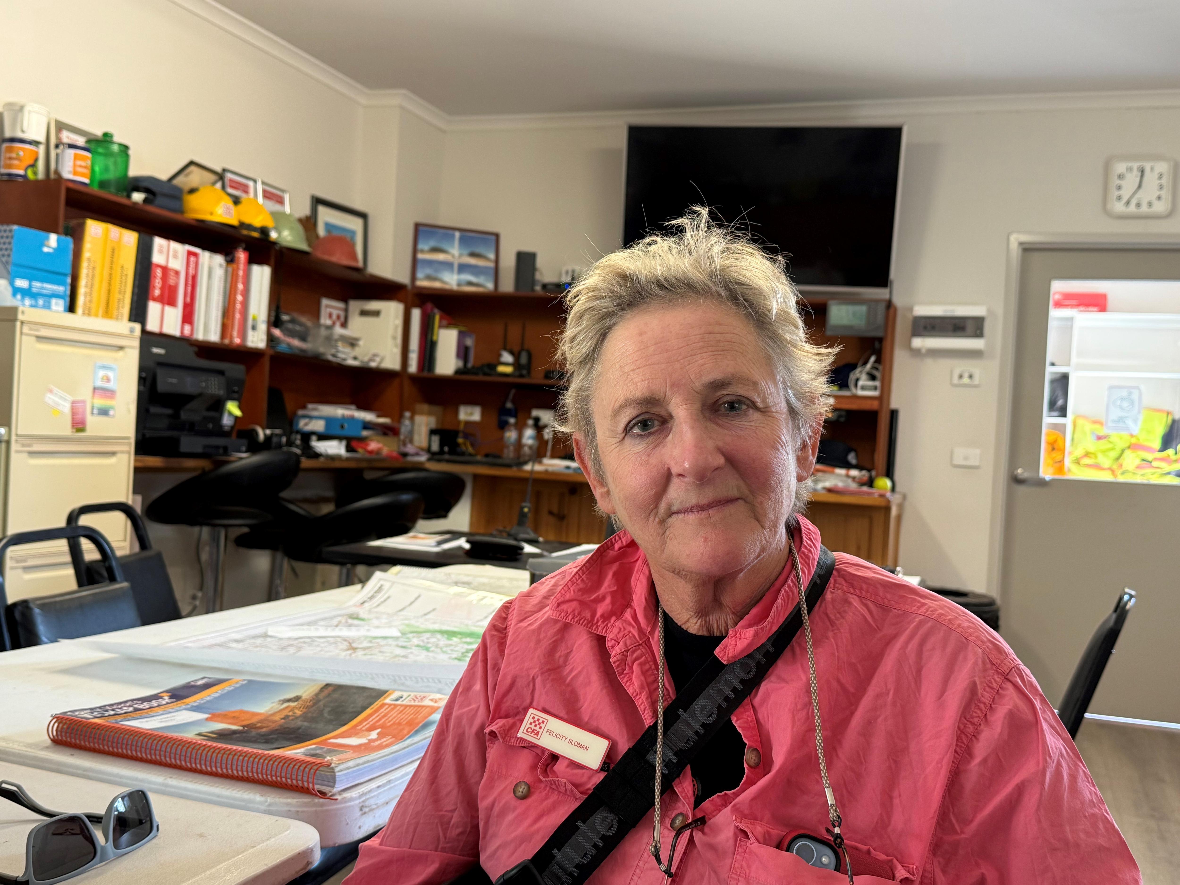Felicity Sloman lleva una camisa rosa con cabello rubio corto y está sentada en una habitación.