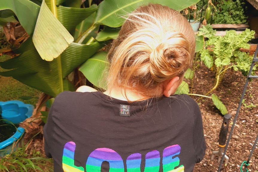 10-year-old girl Ruby crouching down in a garden bed, She is wearing a black t-shirt with the words 'love' written on the back