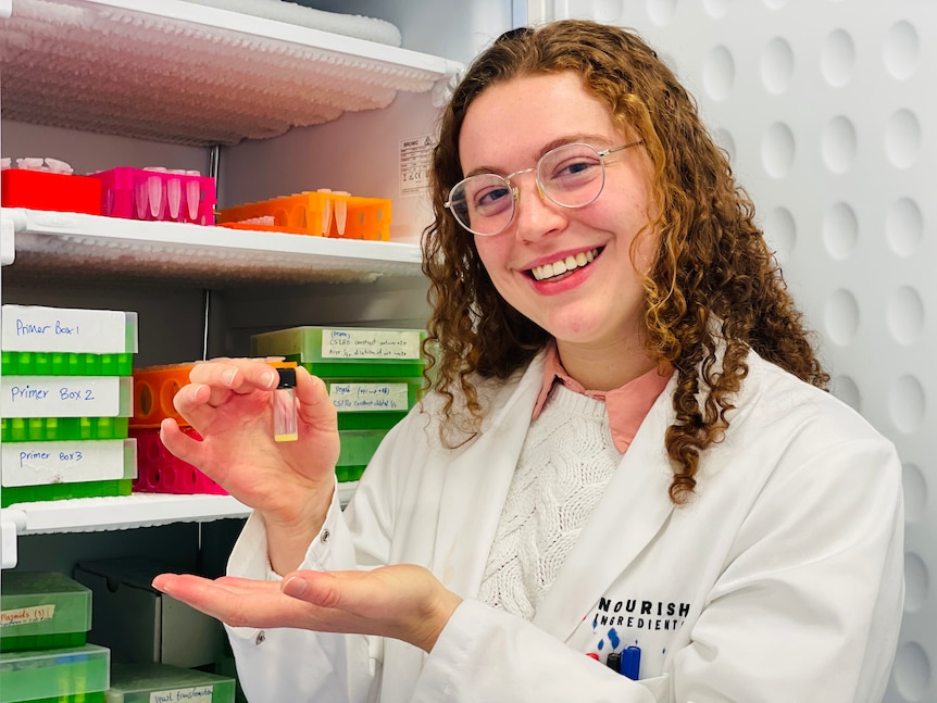 A women wearing a lab coat holding a vial of fat.