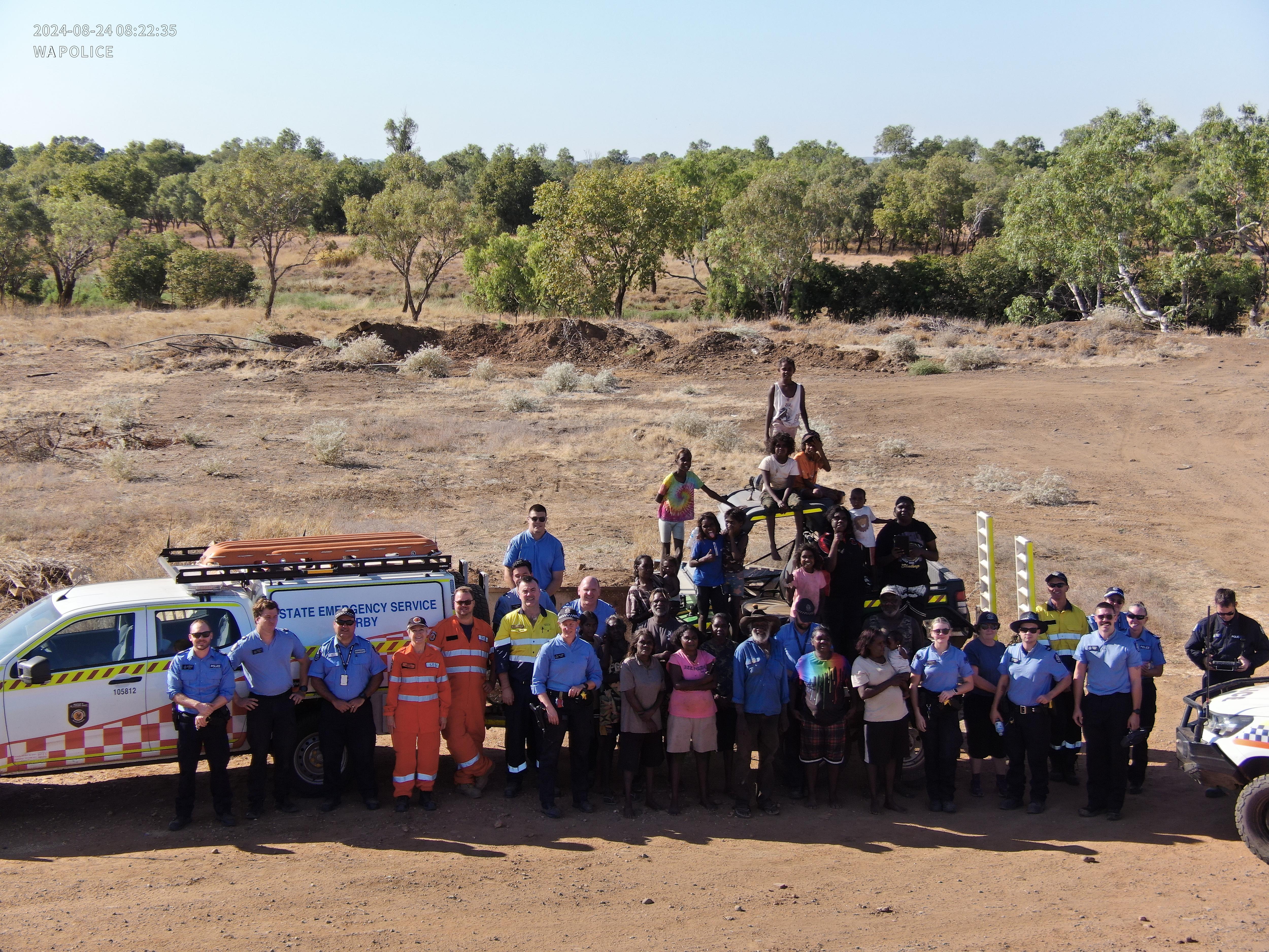 A group of 20 people including police in uniform and community members in front of emergency vehicles